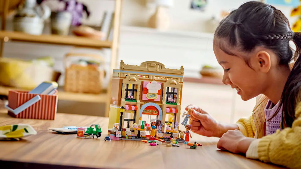 Holčička hrající si se stavebnicí LEGO® Friends 42655 Restaurace a škola vaření u stolu v pokoji_03