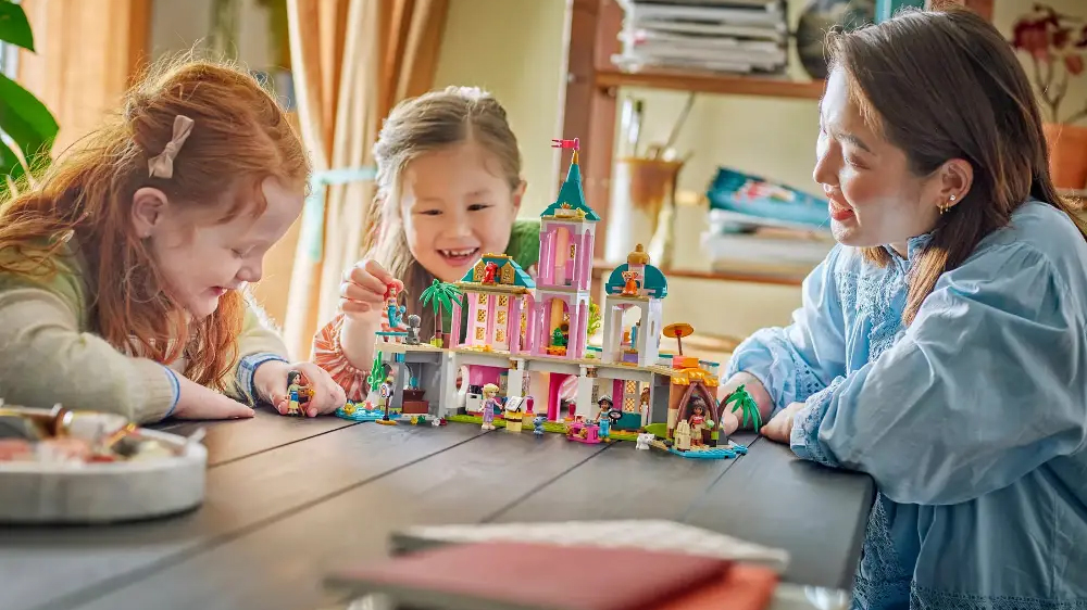Žena se usmívá na 2 dívky, které si hrají s princeznami v hradě ze stavebnice LEGO® Disney_02