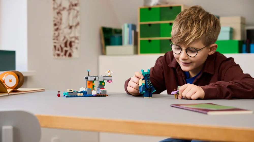 Veselý chlapec si hraje se stavebnicí LEGO® Minecraft® 21274 Setkání se Strážcem a drží v ruce figurky_03