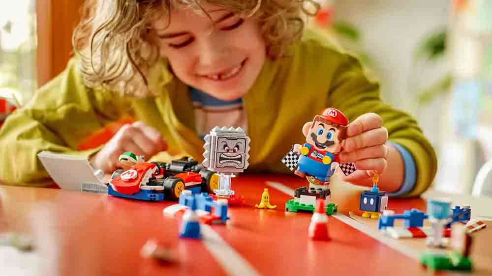 Veselé dítě si hraje se stavebnicí LEGO® Super Mario™ 72043 Mario Kart™ – Interaktivní LEGO® Mario™ a Standard Kart a drží v ruce figurku_02