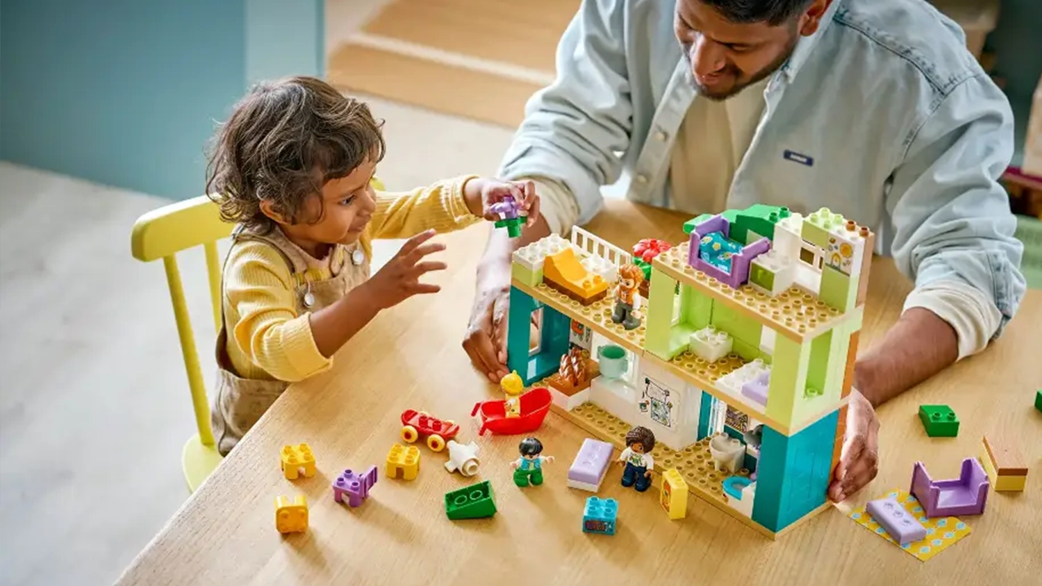 Mal&eacute; d&iacute;tě stav&iacute; domek ze stavebnice LEGO&reg; DUPLO&reg; 10470 Modern&iacute; rodinn&yacute; dům 3v1 s figurkami pod dohledem dospěl&eacute;ho.