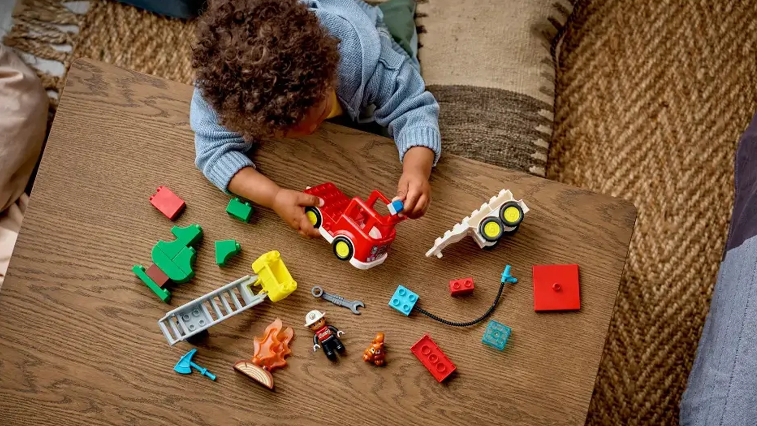 Malý chlapec sestavuje stavebnici LEGO® DUPLO® 10473 Hasičské auto s hadicí a hasičem.