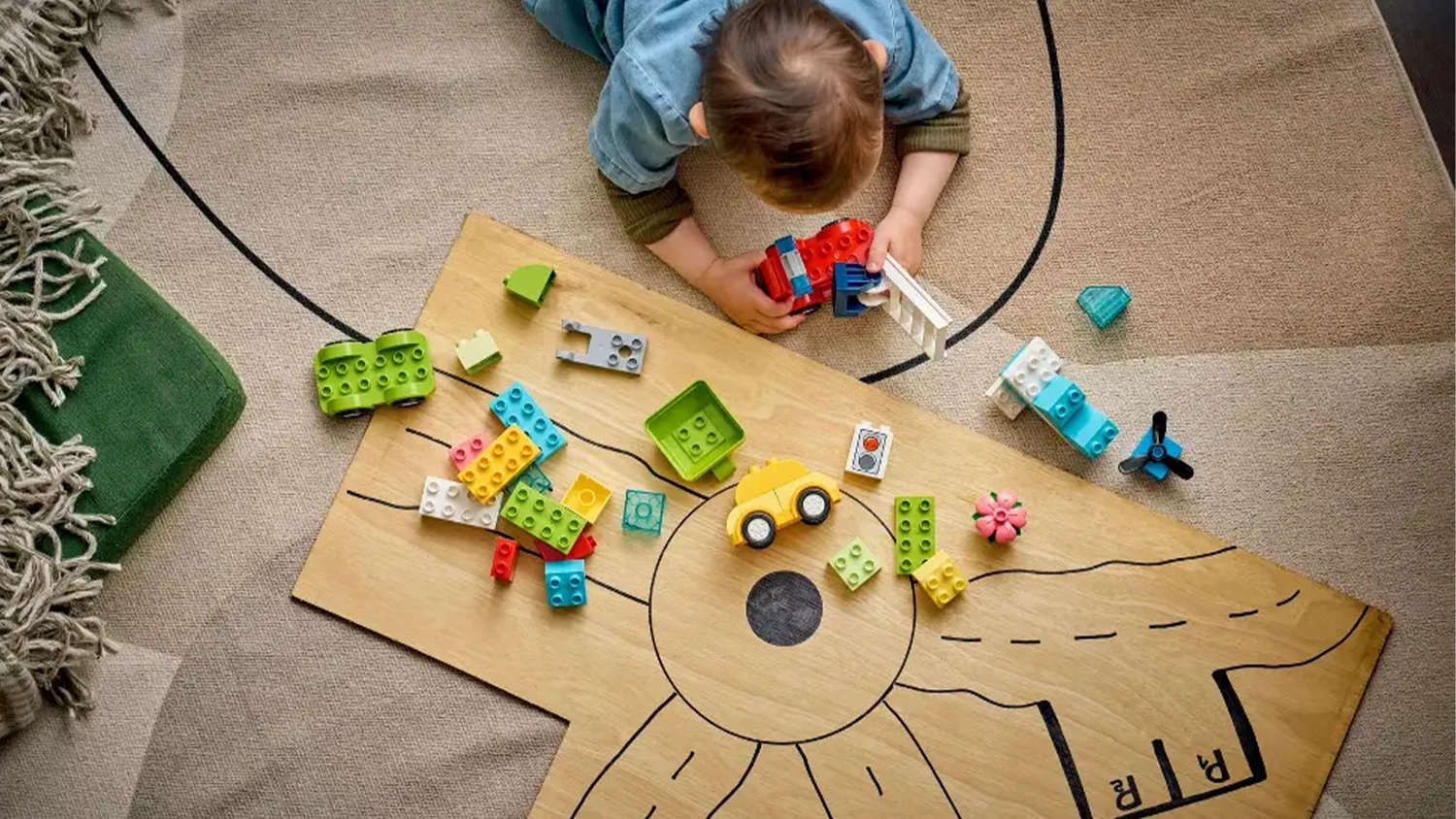 Mal&yacute; chlapec lež&iacute;c&iacute; na koberci sestavuje hasičsk&eacute; auto ze stavebnice LEGO&reg; DUPLO&reg; 10474 Kreativn&iacute; vozidla.