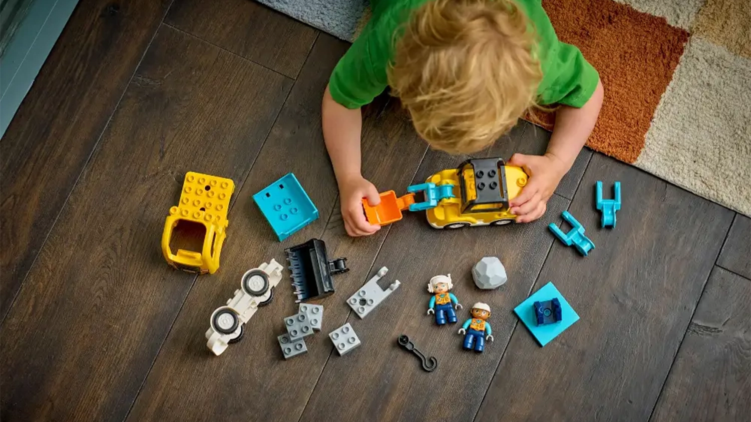 Mal&yacute; chlapec lež&iacute; na dece a sestavuje stavebnici LEGO&reg; DUPLO&reg; Město 10475 Vozidla na stavbě 3v1.