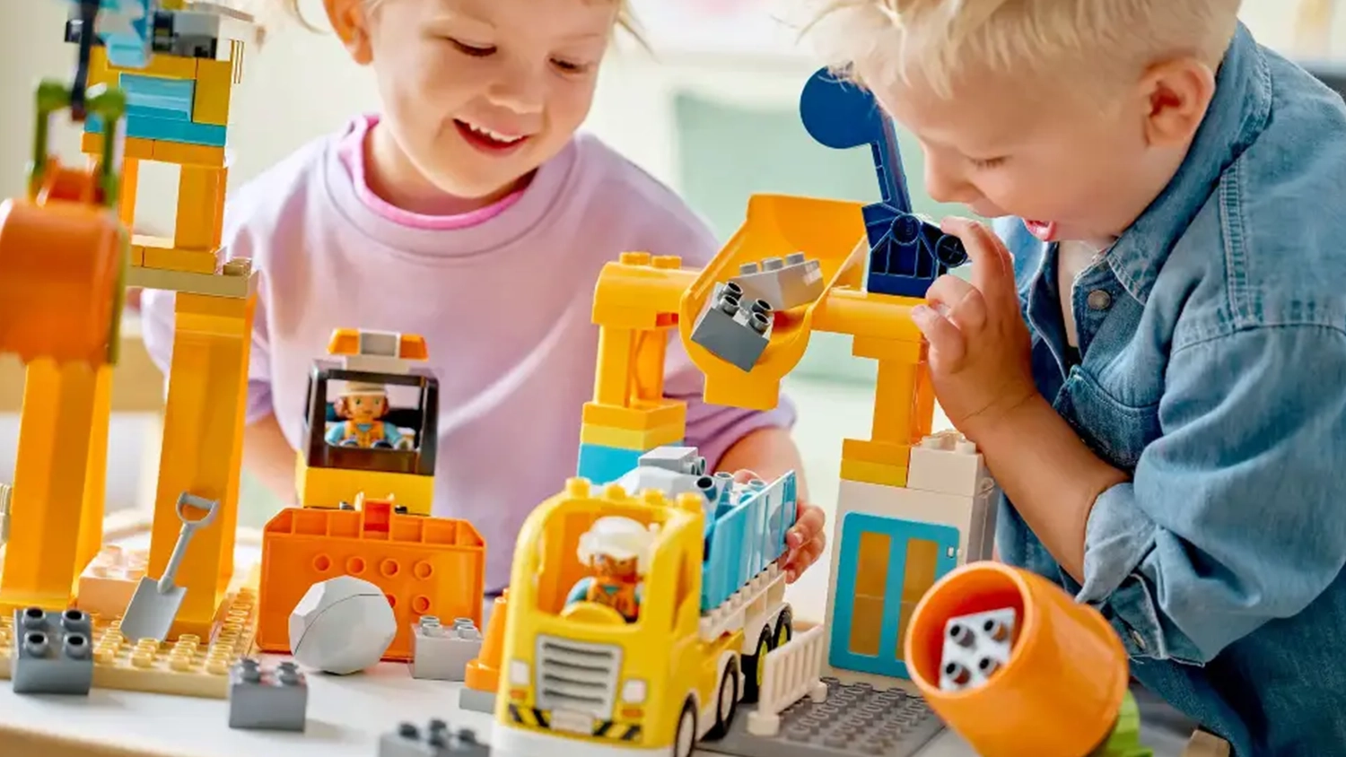 Směj&iacute;c&iacute; se chlapec s holčičkou si hraj&iacute; se stavebnic&iacute; LEGO&reg; DUPLO&reg; Město 10476 Staveni&scaron;tě a vozidla 3v1, chlapec pos&iacute;l&aacute; kostky do n&aacute;klaď&aacute;ku.