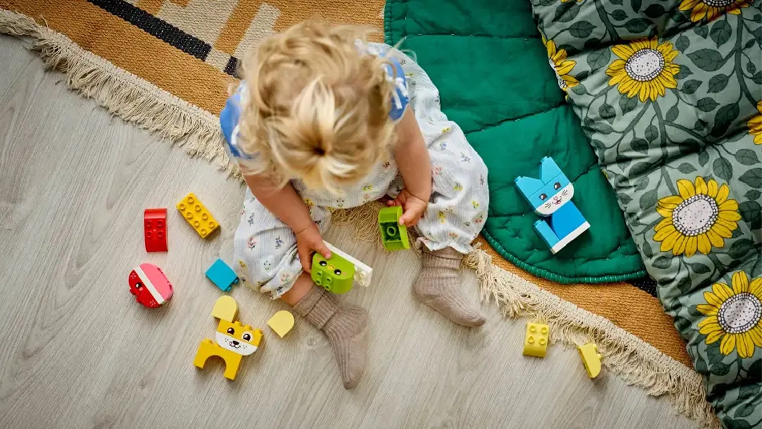 Holčička sed&iacute;c&iacute; na koberci sestavuje figurky ze stavebnice LEGO&reg; DUPLO&reg; 10477 Roztomil&iacute; kreativn&iacute; mazl&iacute;čci 3v1.