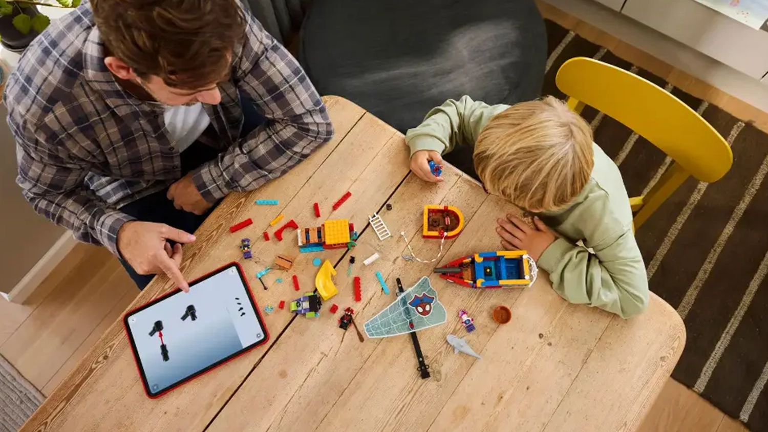 Muž kouk&aacute; na manu&aacute;l v aplikaci LEGO&reg; Builder a pom&aacute;h&aacute; chlapci se stavěn&iacute;m stavebnice Pir&aacute;tsk&aacute; loď Spideyho t&yacute;mu (11208).