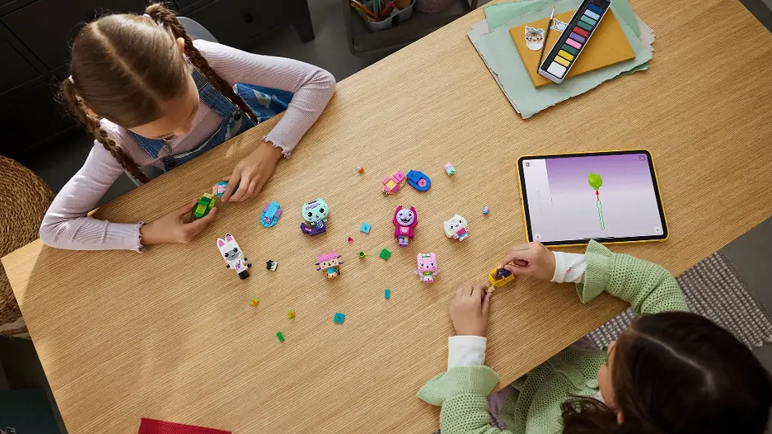 Dve dievčatá skladajú figúrky zo stavebnice LEGO® Gabby’s Dollhouse 11215 Gabby a mačací kamaráti z kociek a používajú manuál v aplikácii LEGO® Builder.