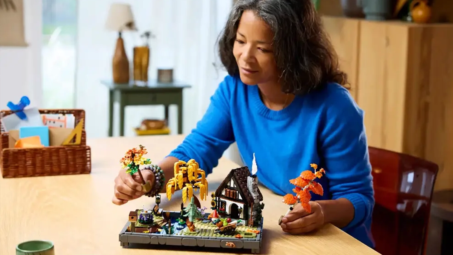 Žena přemýšlí, kam umístí stromy v zahradě ze stavebnice LEGO® Icons 11372 Chata a podzimní zahrada.