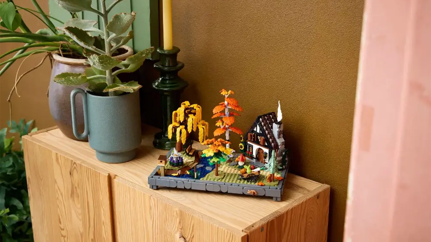 Stavebnice LEGO® Icons 11372 Chata a podzimní zahrada vystavená na skříňce vedle svíčky a rostlin