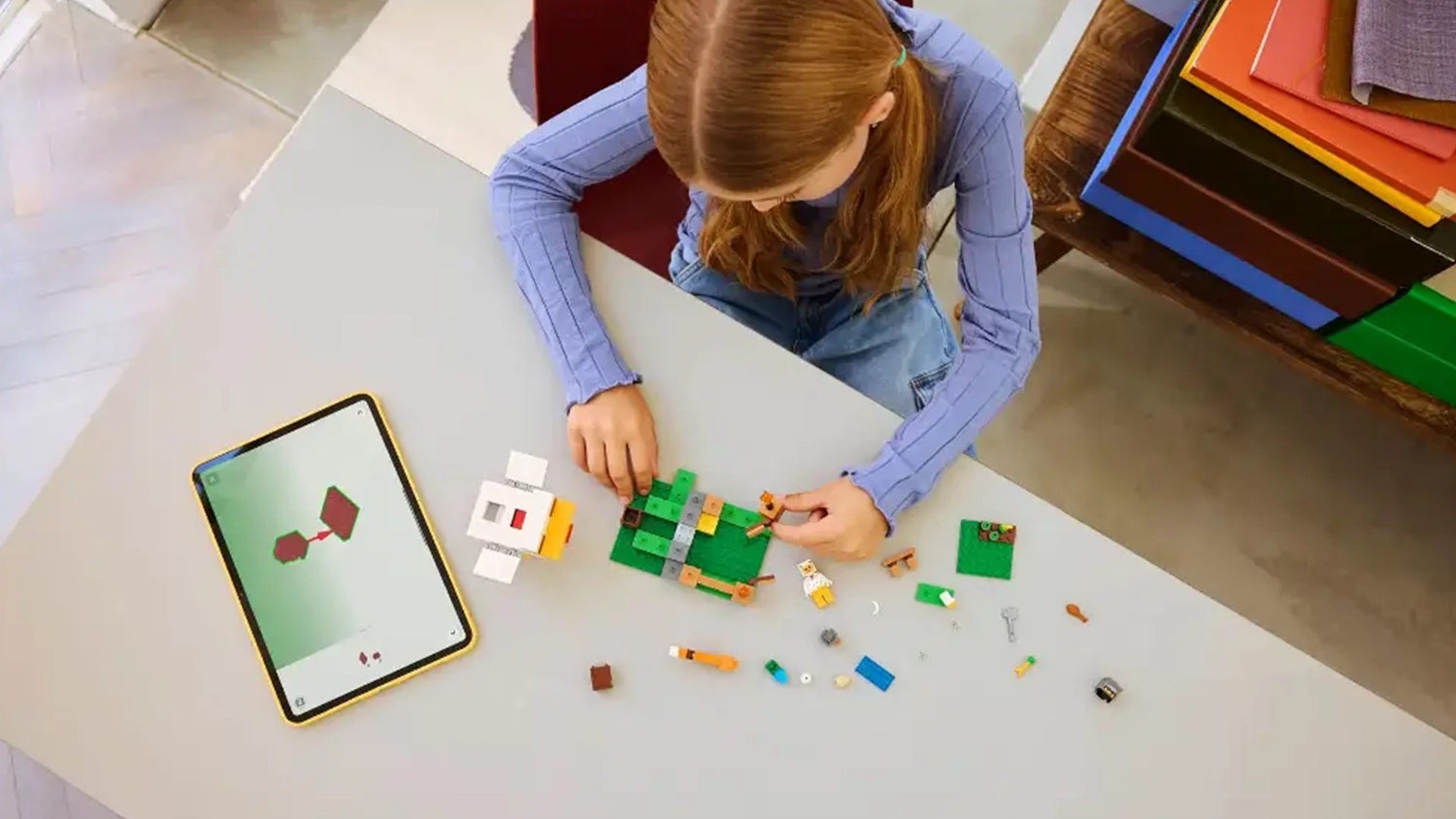 Dívka skládá stavebnici LEGO® Minecraft® 21585 Slepičí farma s pomocí návodu v aplikaci LEGO® Builder na tabletu.