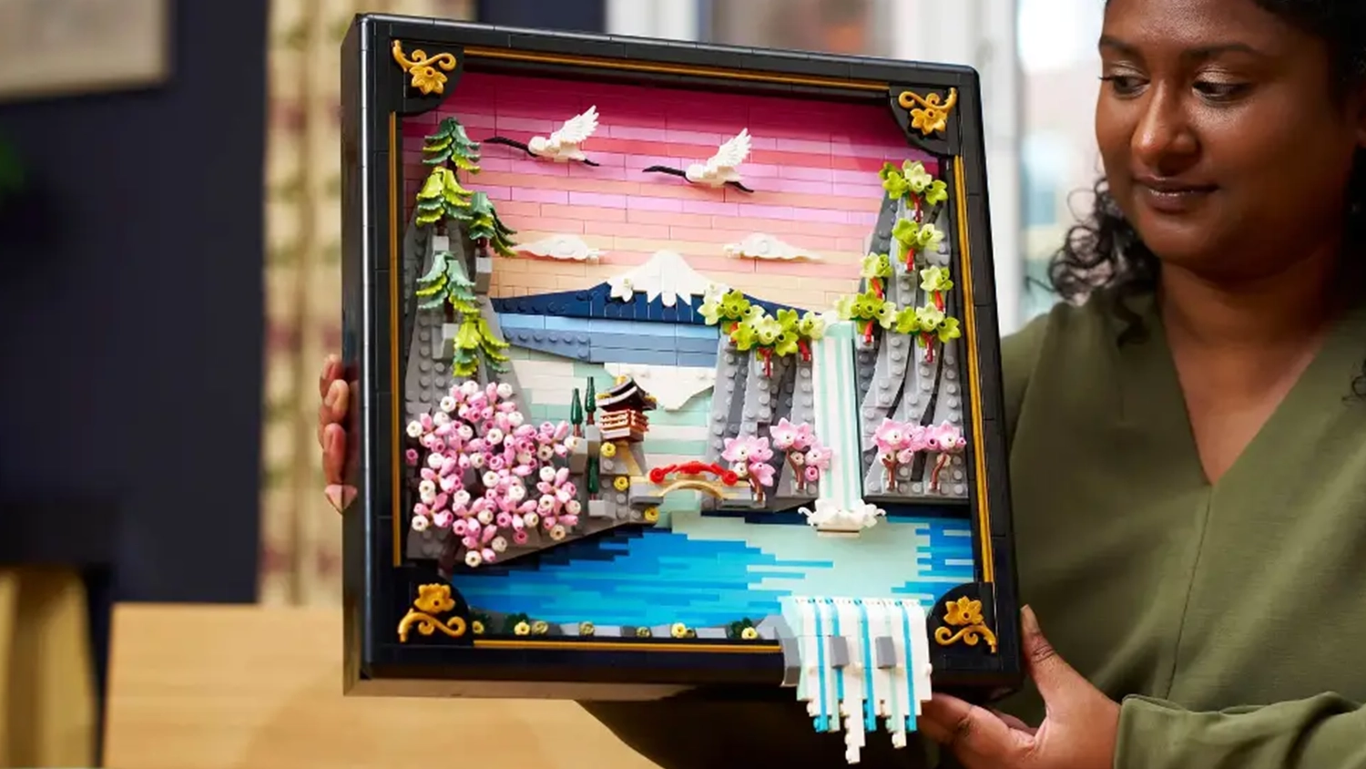 Usm&iacute;vaj&iacute;c&iacute; se žena drž&iacute; v rukou hotov&yacute; obraz ze stavebnice LEGO&reg; Art 31218 Krajina se sakurami