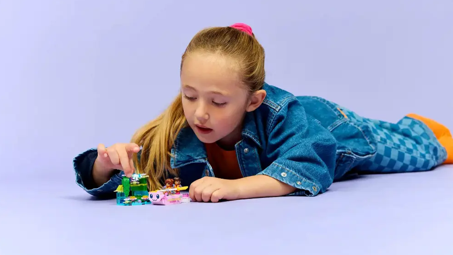 Děvč&aacute;tko lež&iacute; na zemi a hraje si se stavebnic&iacute; LEGO &reg;