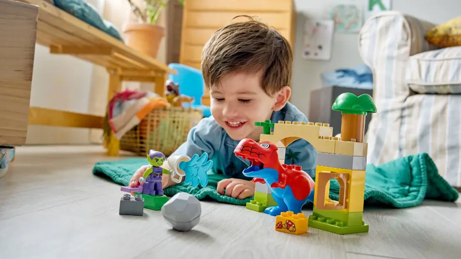 Vesel&yacute; chlapec lež&iacute; na dece a hraje si se stavebnic&iacute; LEGO&reg; DUPLO&reg; Marvel 10463 Dinosaurus Spidey-Rex vs. Zelen&yacute; goblin.
