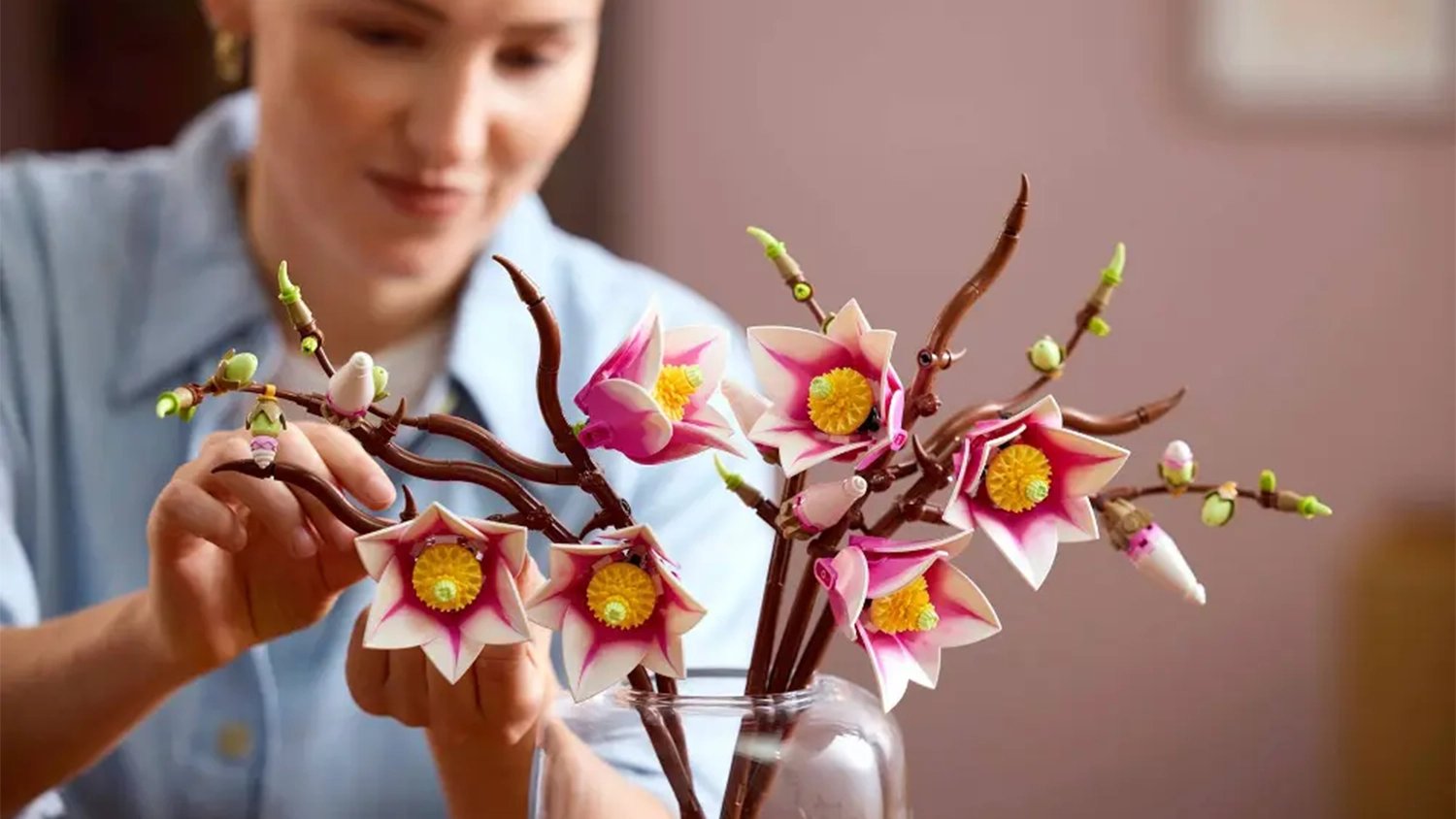 Usmievajúca sa žena aranžuje vetvičky magnólie zo stavebnice LEGO® Botanicals (11510) vo váze.