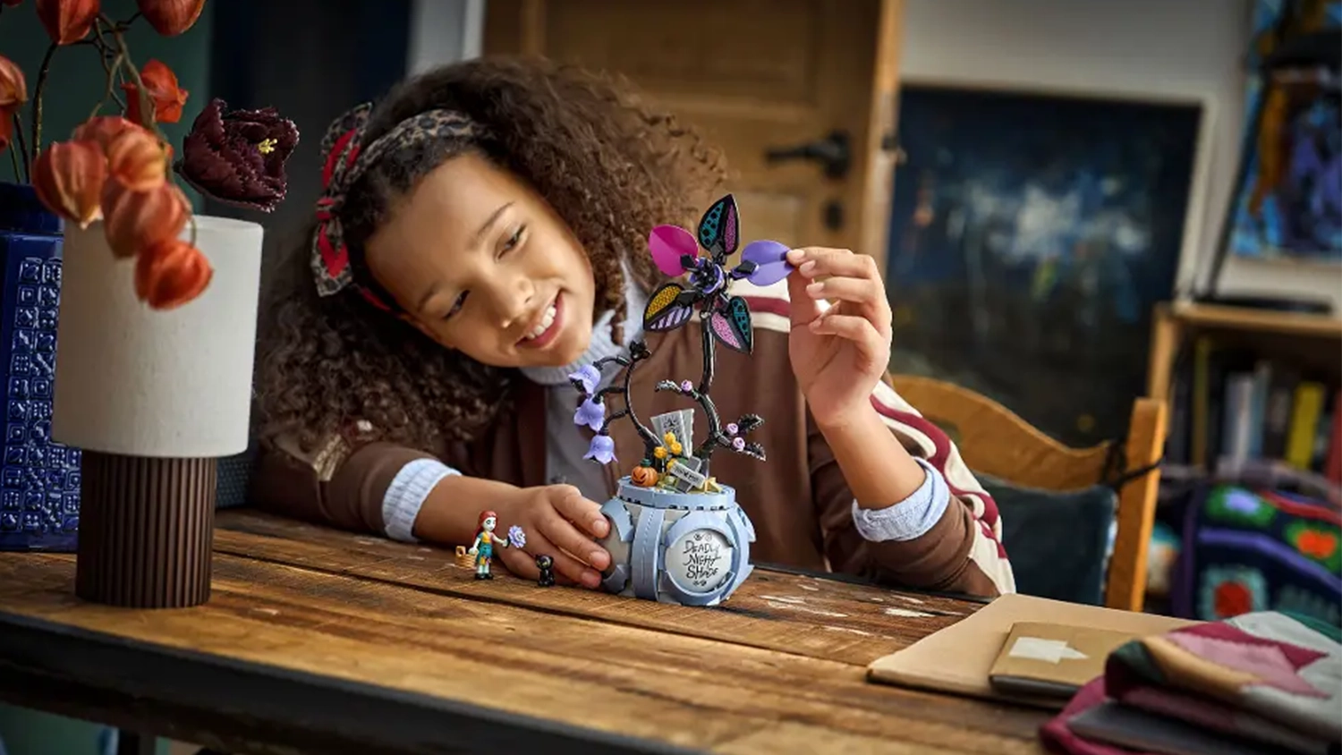 Dievča s úsmevom obdivuje stavebnicu LEGO® | Disney 43288 Sallyin kvetináč vystavenú na stole.