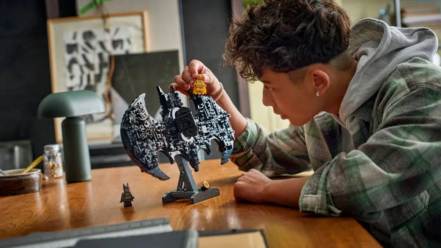 Mladý kluk obdivuje stavebnici LEGO® DC Batman™ 76330 Logo Batman™ a drží v ruce zlatou minifigurku Batmana.