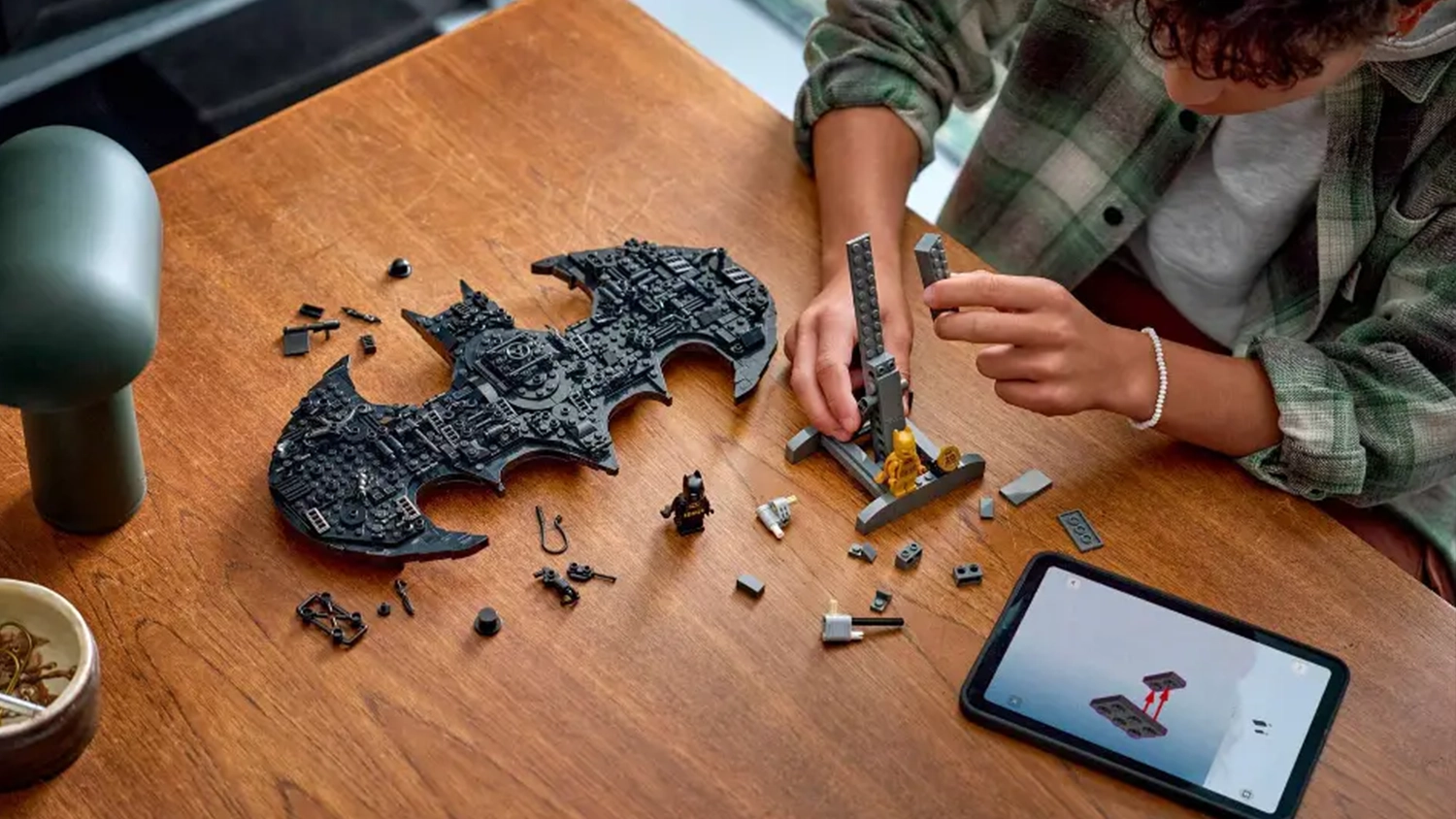 Chlapec sestavuje stavebnici LEGO® DC Batman™ 76330 Logo Batman™ a má otevřený návod v aplikaci LEGO® Builder na tabletu.