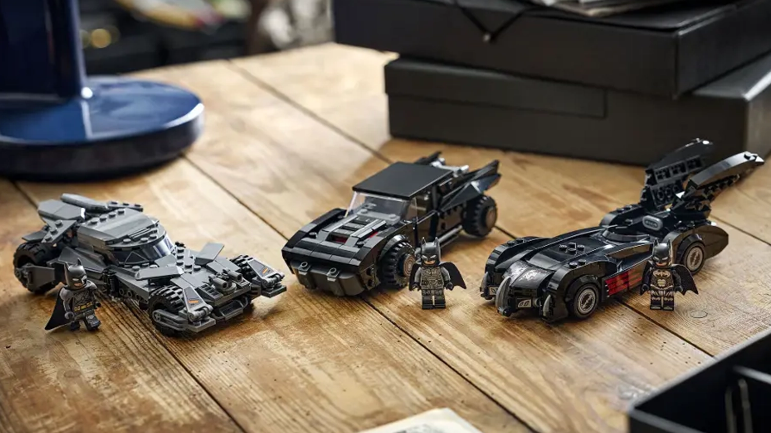 Tři repliky Batmobilů ze stavebnice LEGO&reg; DC Batman&trade; a 3 minifigurky Batmana vystaven&eacute; na stole