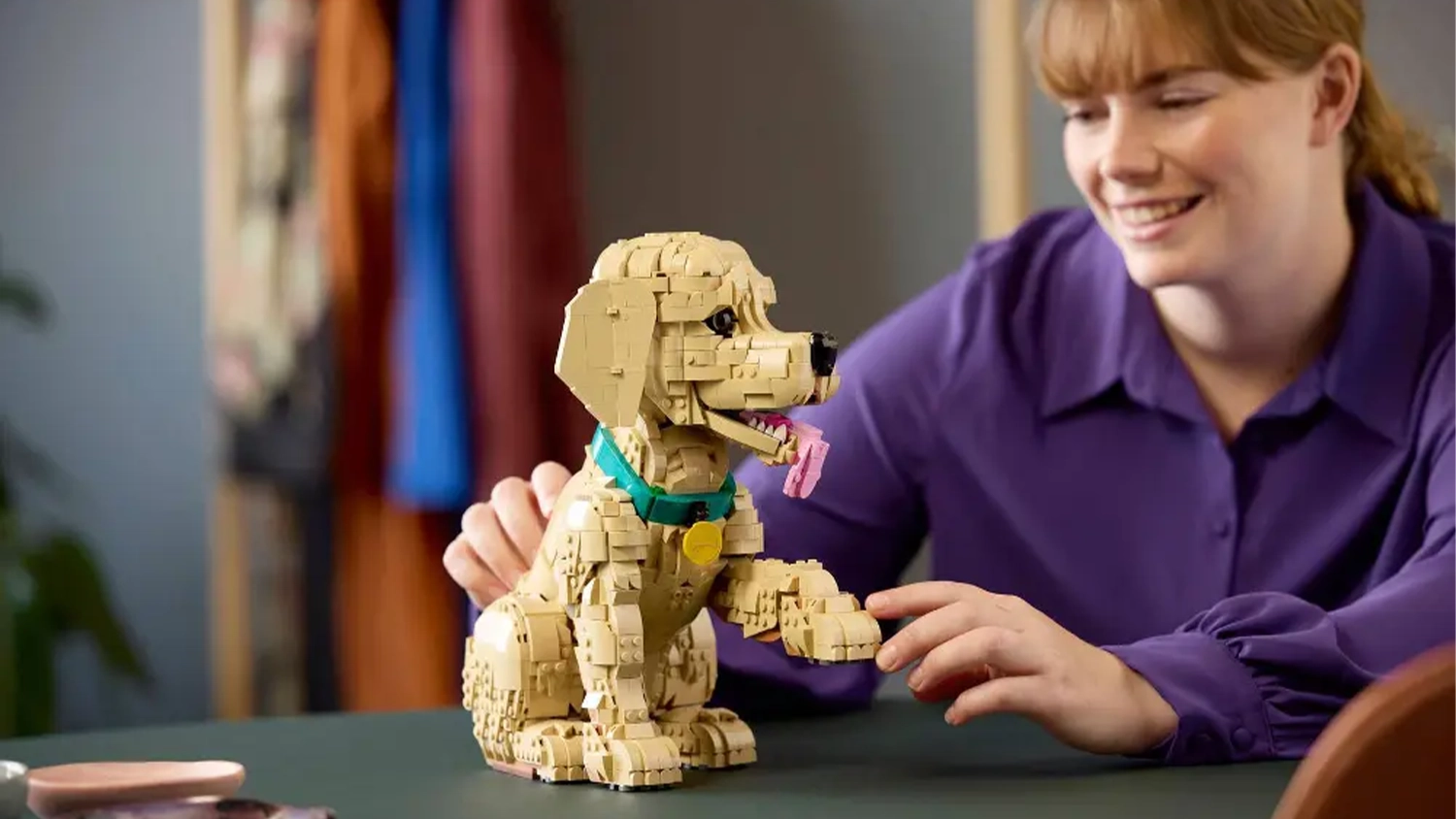 Veselá žena sa hrá s modelom šteniatka zlatého retrievera zo stavebnice LEGO® Icons (11384).