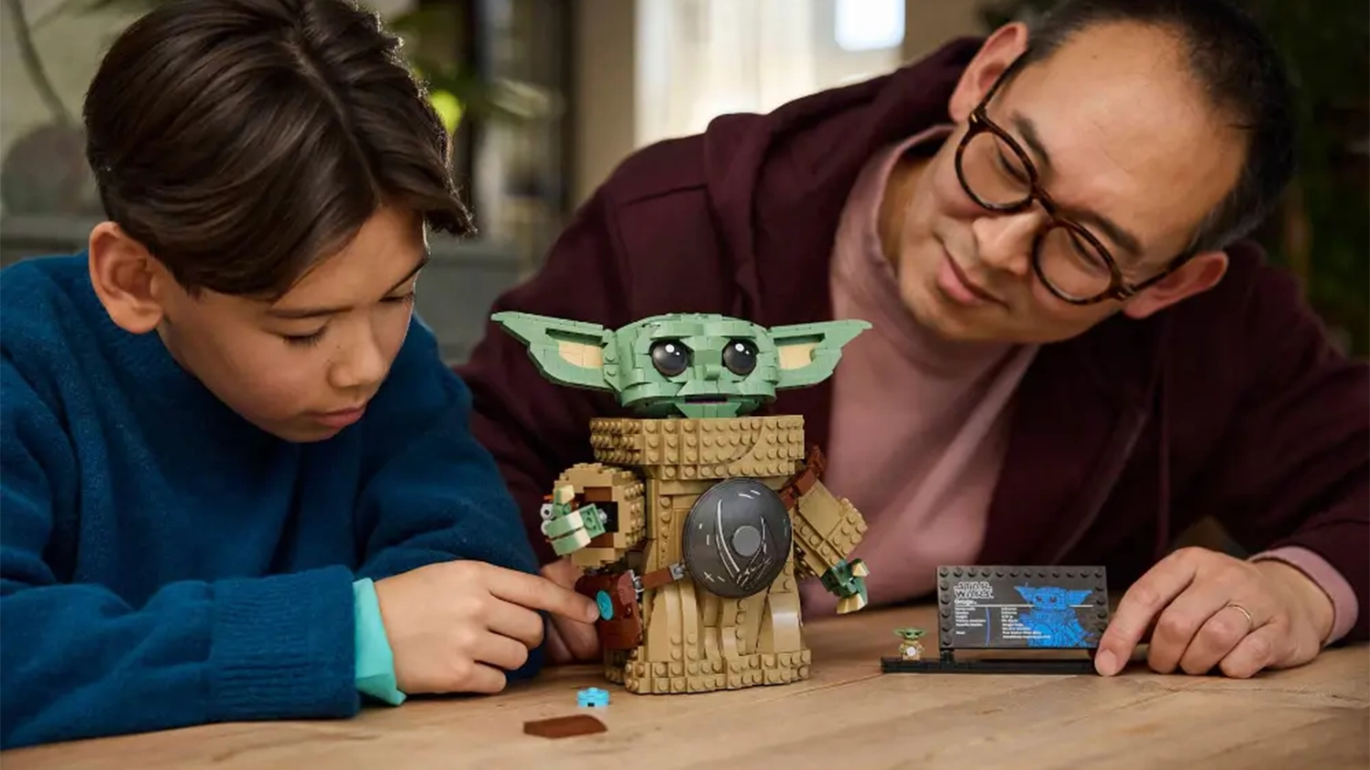 Otec se synem sedí u stolu a s úsměvem obdivují hotovou stavebnici LEGO® Star Wars™ 75446 Grogu™ (mandalorianský učedník).