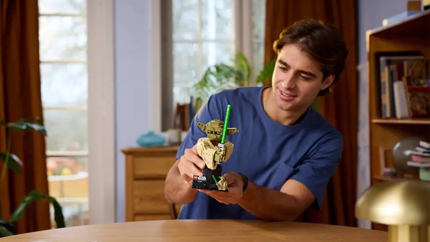 Muž se usm&iacute;v&aacute; na bustu Yody ze stavebnice LEGO&reg; Star Wars&trade; (75438), kterou drž&iacute; v rukou.