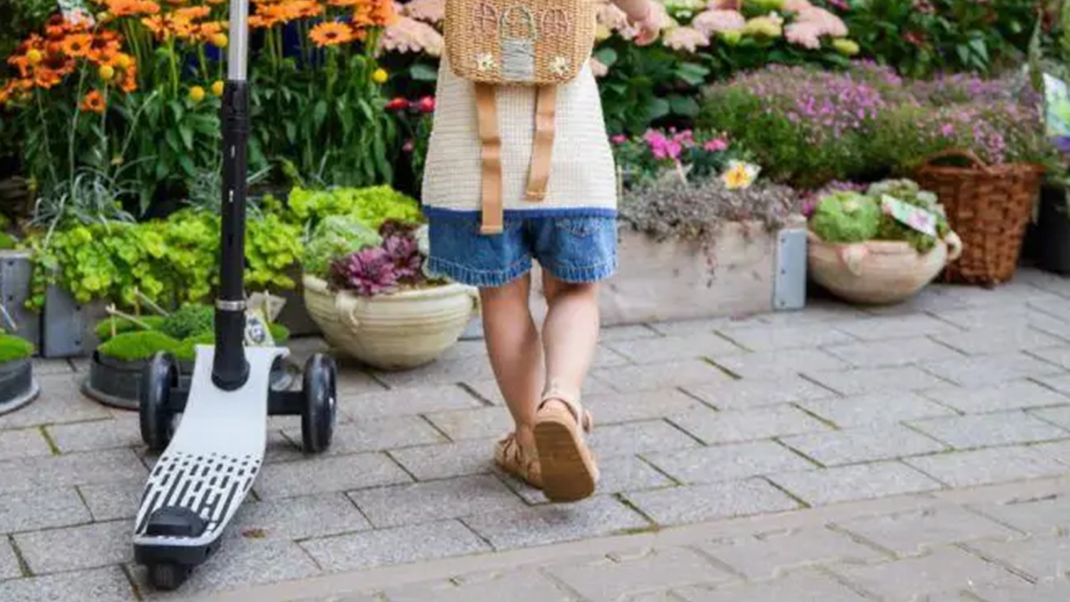 Dievčatko s prilbou zastavilo na ulici na kolobežke MoMi SAN pri truhl&iacute;koch s kvetmi