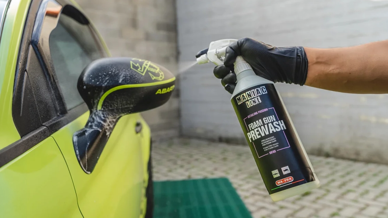 Ruka v gumovej rukavici nastrieka akt&iacute;vnu penu MANIAC Foam Gun Prewash 1 000 ml (MF-88) na sp&auml;tn&eacute; zrkadlo automobilu
