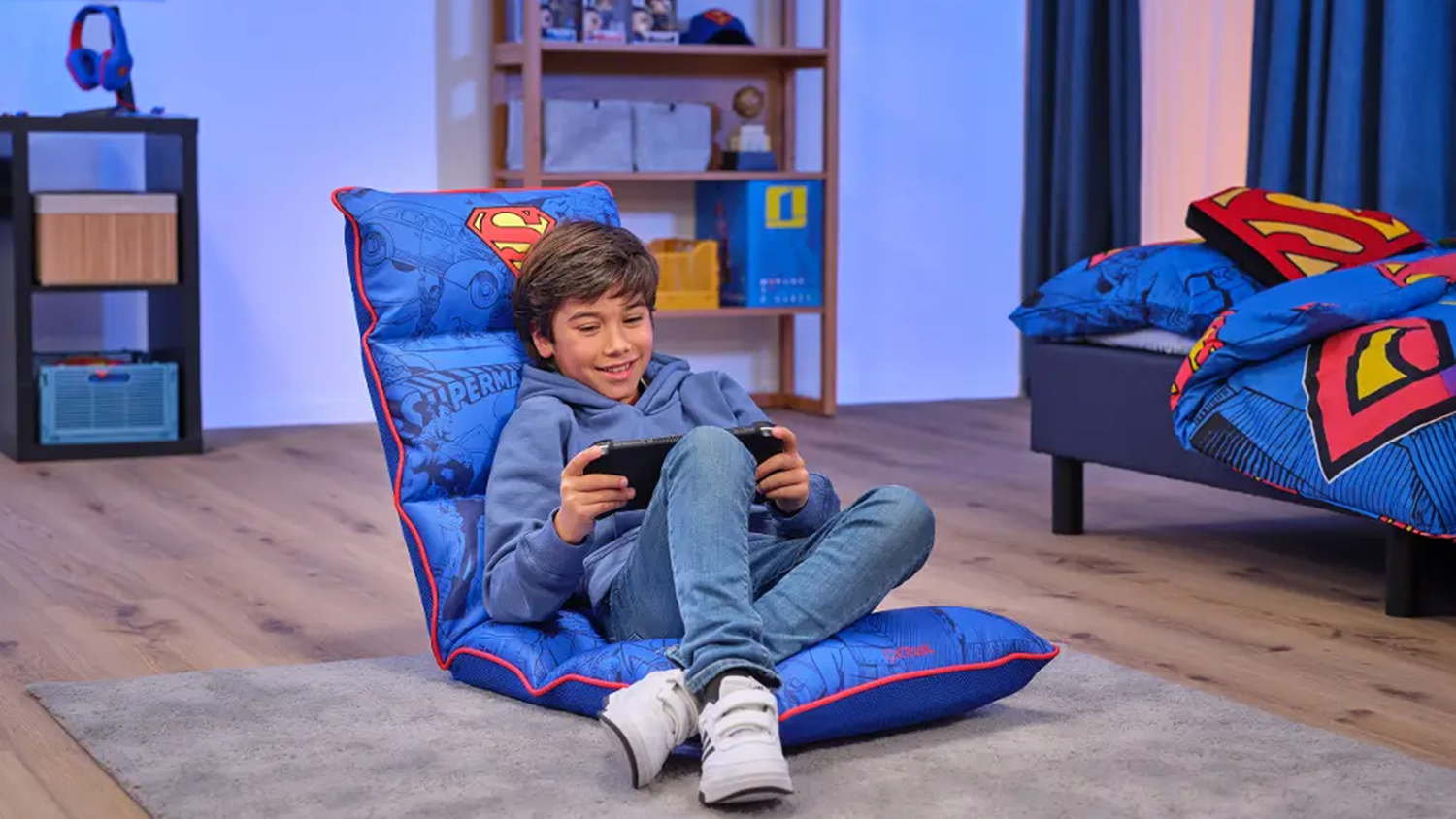 Chlapec sedí na podlahovej hernej stoličke Trust GXT 718SM Rayzee Foldable Superman