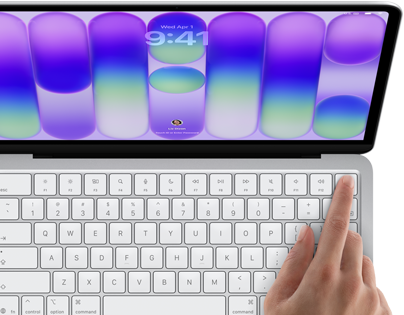 MacBook Neo v striebornej farbe zobrazuje prihlasovaciu obrazovku, niečí prst na senzore Touch ID v pravom hornom rohu klávesnice