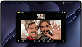 Stříbrný MacBook Pro s PROLED XDR displejem, zobrazuje se probíhající videohovor se dvěma lidmi, kteří jsou v prosluněném městě a mávají osobě doma