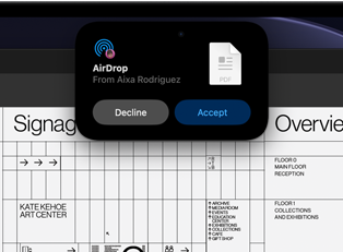 Na obrazovce je vidět Dynamic Island s žádostí o přenos přes AirDrop, má podobu malého okna, které překrývá část otevřeného souboru Adobe Acrobatu