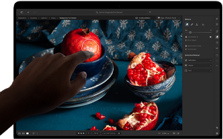 MacBook Pro s PROLED XDR displejem, na kterém je zátiší s granátovými jablky, modrou keramikou a textiliemi, k displeji se natahuje ruka, aby s uměleckým dílem interagovala